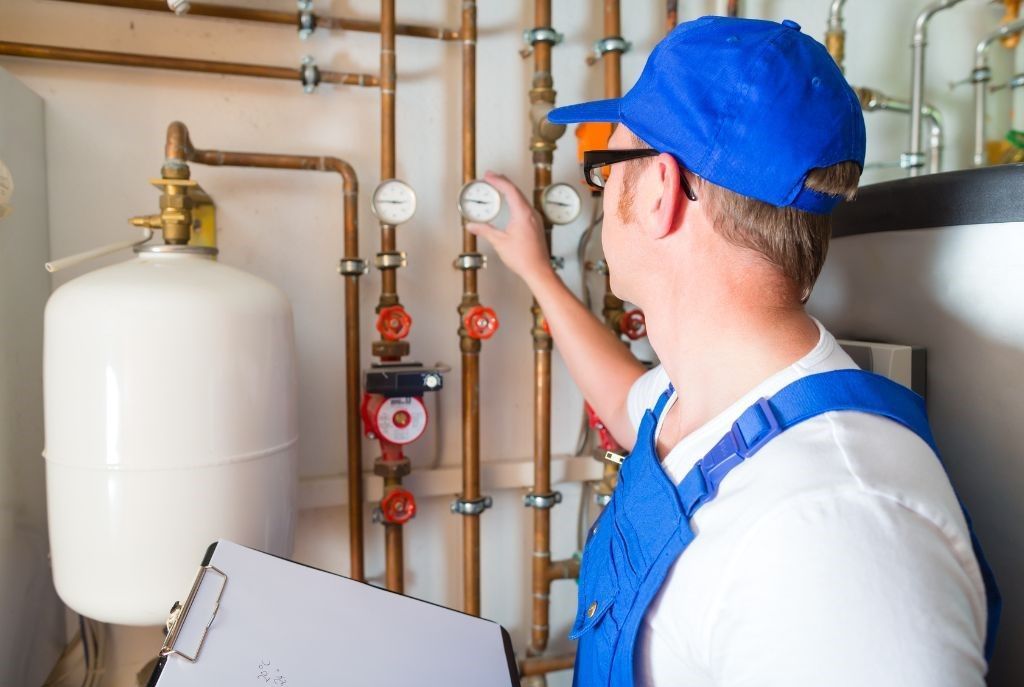 A man in a blue hat is working on a pipe while holding a clipboard.