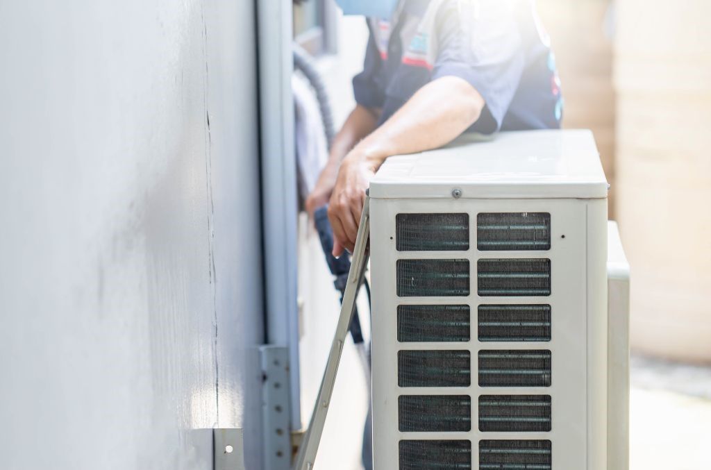A man is installing an air conditioner on the side of a building.