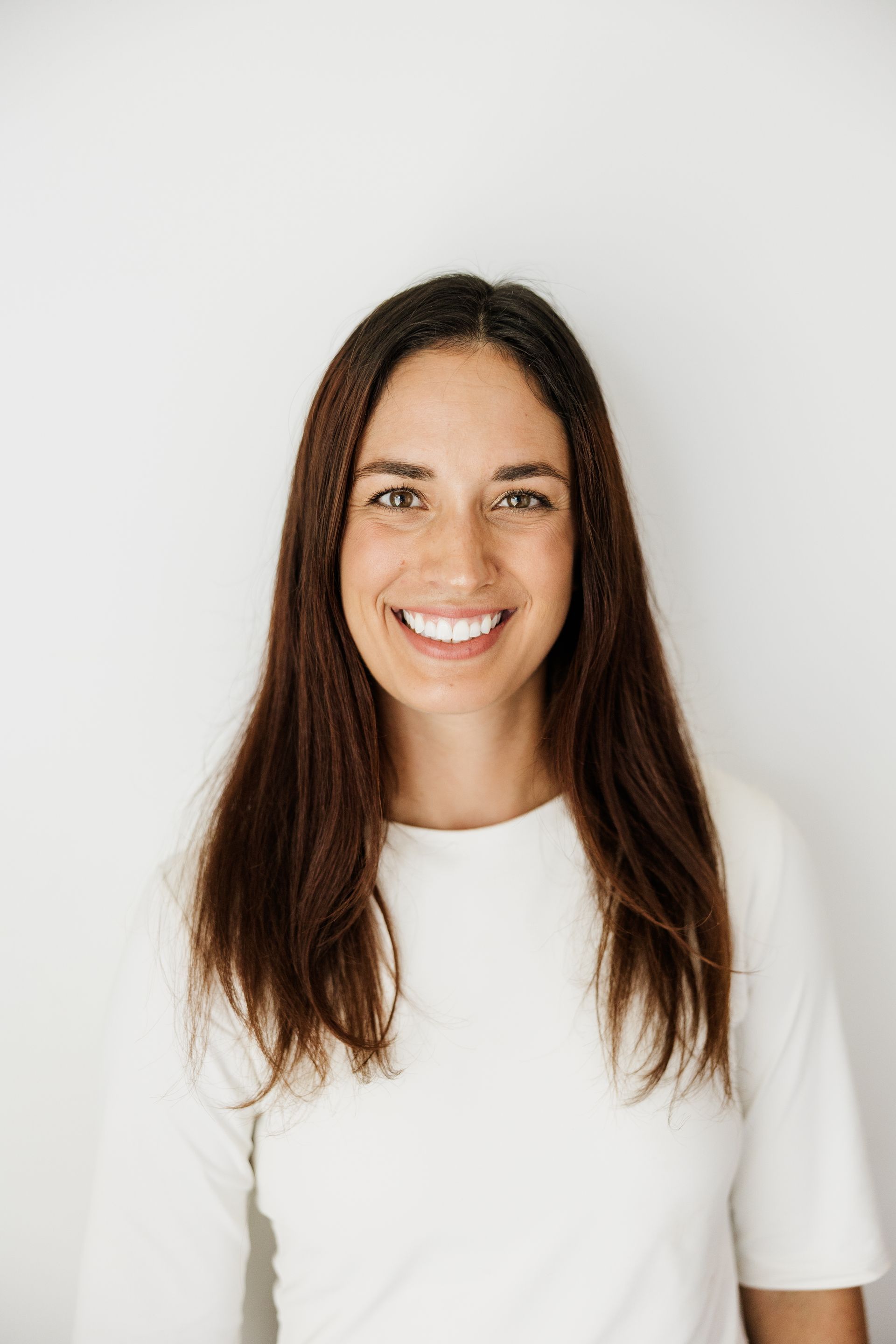 Dr. Chloe smiles with long dark hair wearing a white shirt against a plain white background