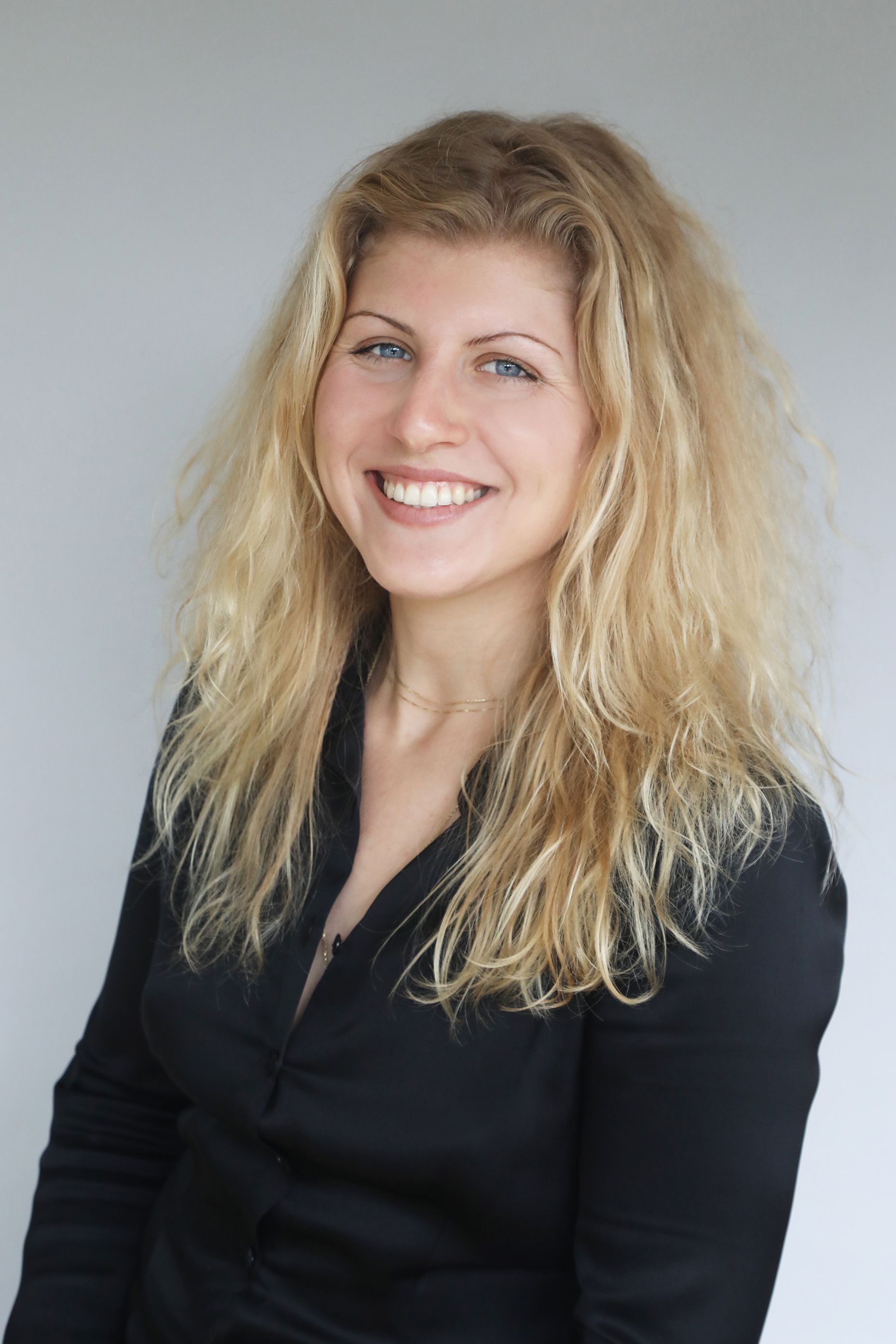 Galina Perekrestova smiles in a black blazer posing against a light gray background