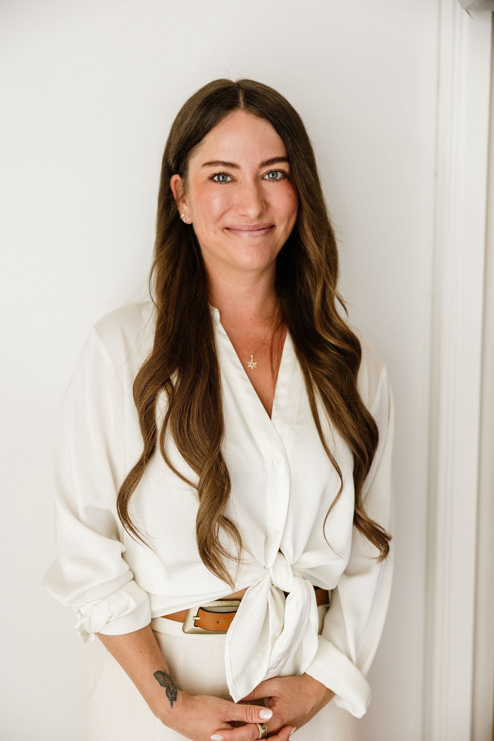 Dr. Julie Soloduka in a white blouse and pants, smiling against a light wall.