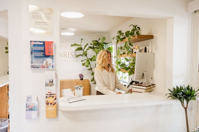 Woman at a bright white reception desk in a plant-filled office lobby.