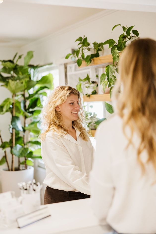 A patient checks in for her chiropractic appointment in a bright office with a desk with many green plants.