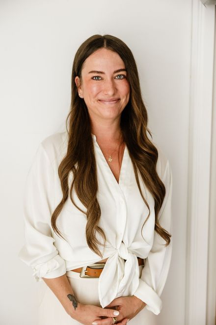 Dr. Julie Soloduka in a white blouse and pants, smiling against a light wall.