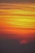 Orange and yellow sunset sky over a dark horizon, with thin clouds and a faint red sun.