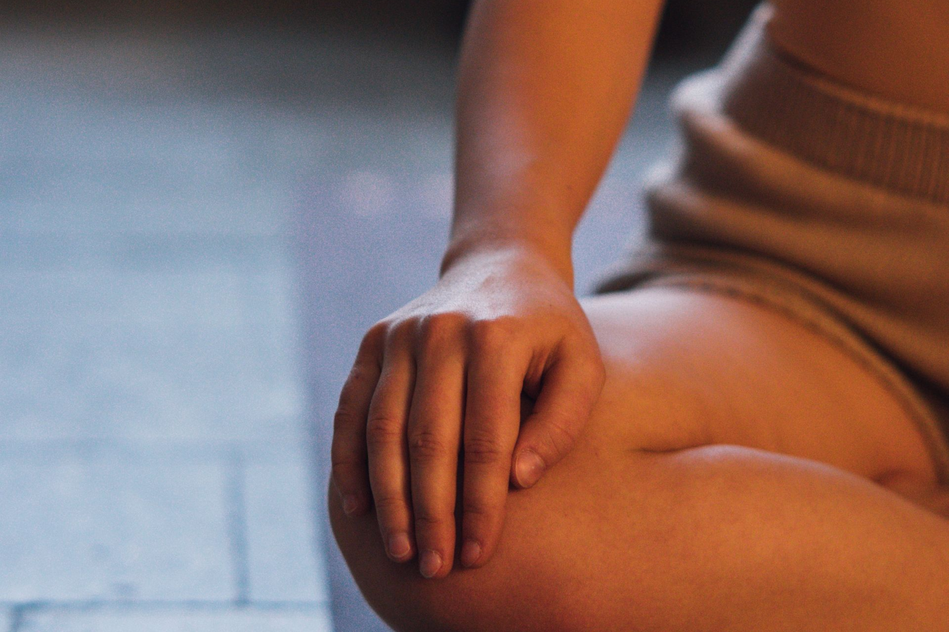 Hand resting on a bare knee, lit by warm indoor light on a blurred floor background
