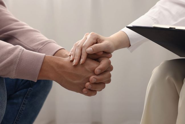 Two people clasping hands in a counseling session, one holding a black folder.