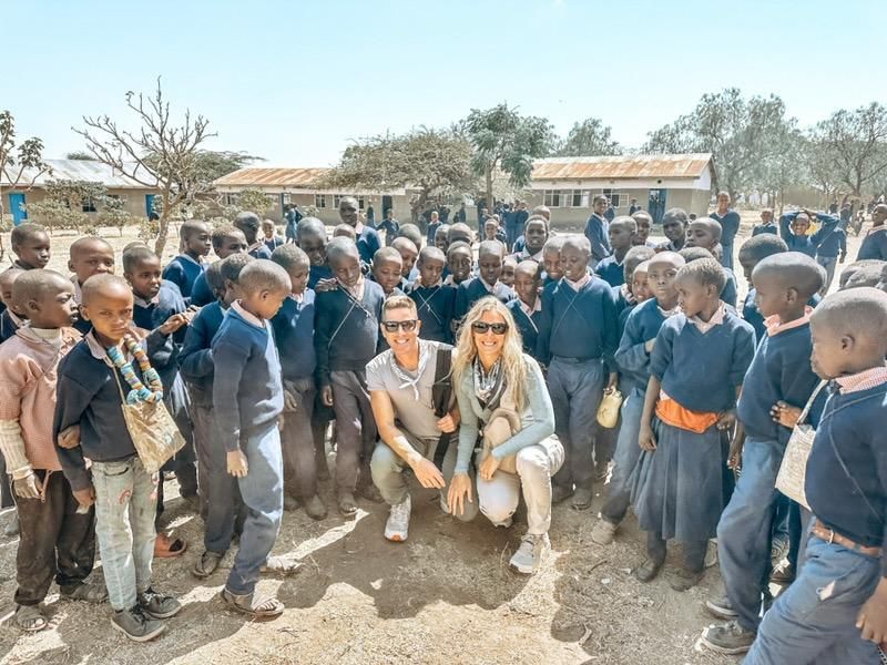 Group of children and two adults posing outdoors in a dusty village courtyard,