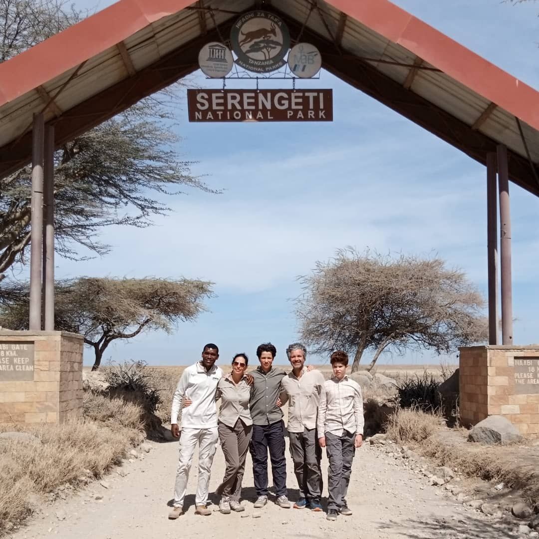 Five people standing under the Serengeti Auto Park entrance arch on a dusty road.