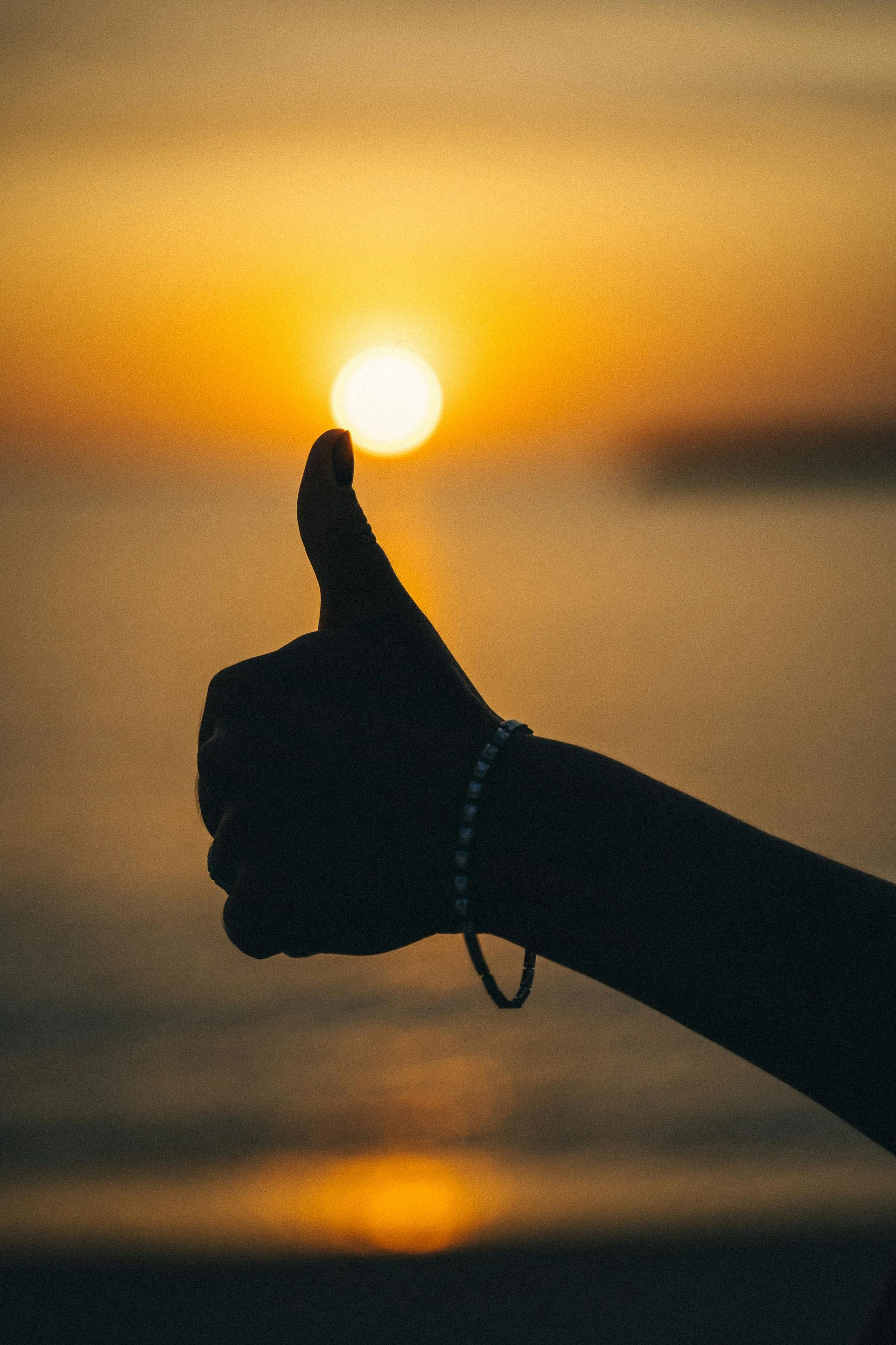 Silhouette of a hand giving a thumbs-up against a sunset over water