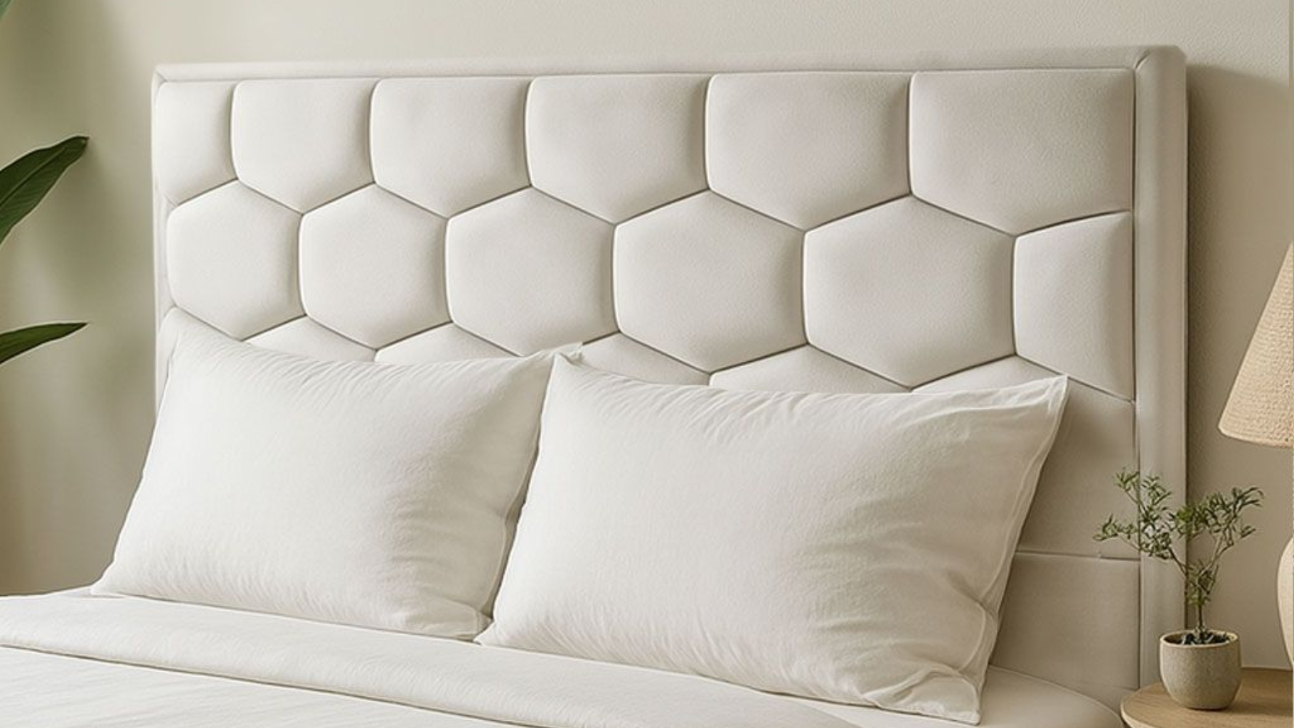 Cama blanca con almohadas grandes y cabecero acolchado geométrico en un dormitorio suave y neutro.