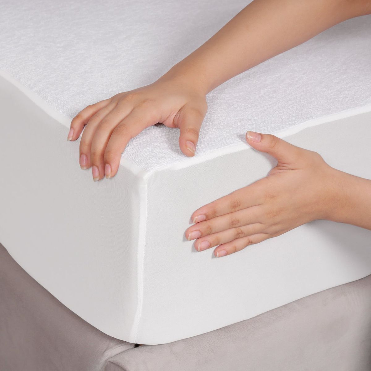 Manos colocando un cubrecolchón de espuma blanca sobre una cama.