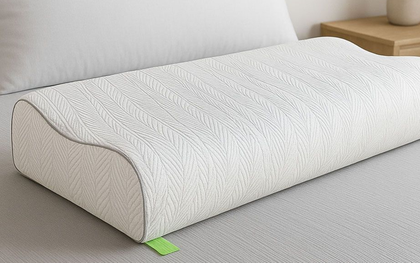 Almohada de espuma gris sobre una cama en un dormitorio, con una mesita de noche de madera al fondo.