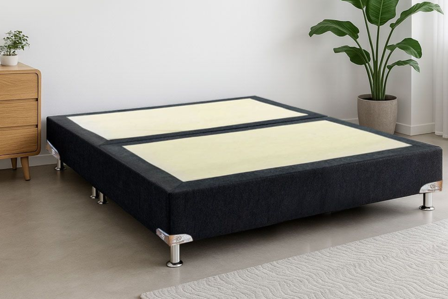 Cama baja negra con plataforma y paneles de colchón beige en una habitación minimalista con planta y mesita de noche.