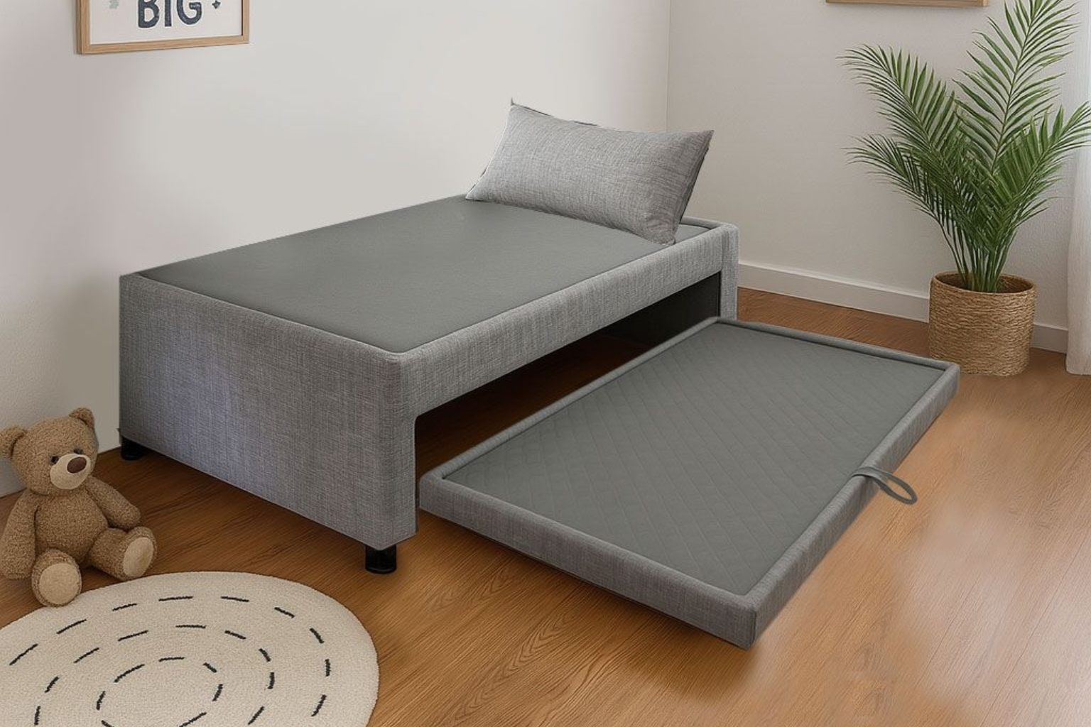 Sofá cama gris con cama nido extraíble en una habitación luminosa, junto a una planta y un osito de peluche sobre un suelo de madera.