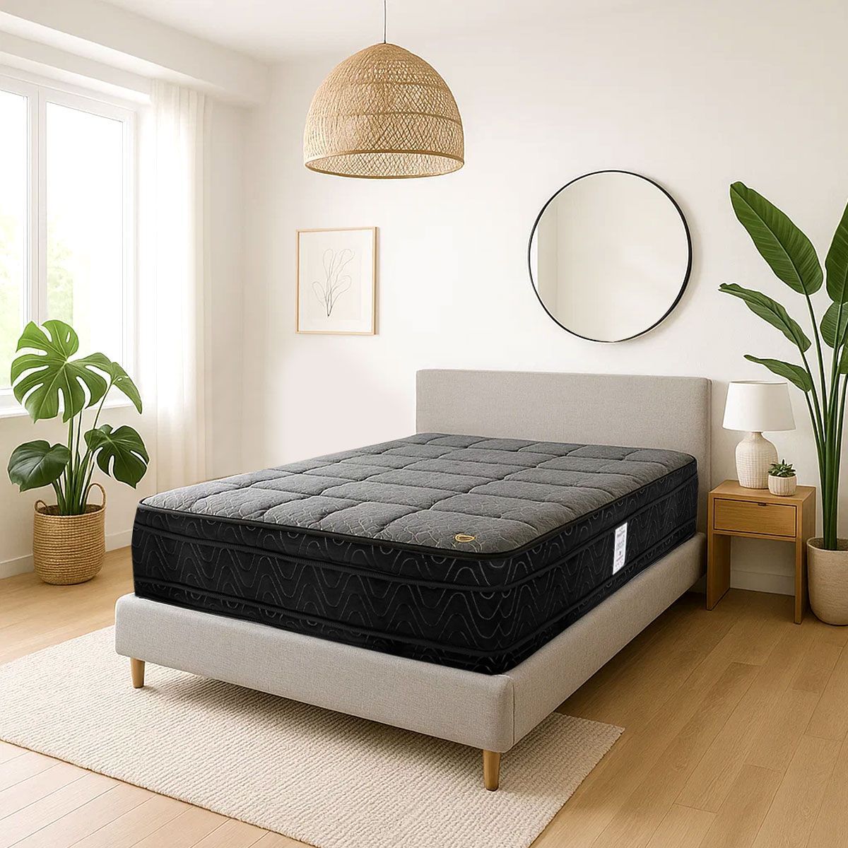 Dormitorio minimalista con colchón negro, estructura de cama beige, espejo redondo, plantas y lámpara colgante de mimbre.