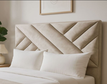 Cabecero tapizado en color beige con costuras geométricas detrás de almohadas y ropa de cama blancas.
