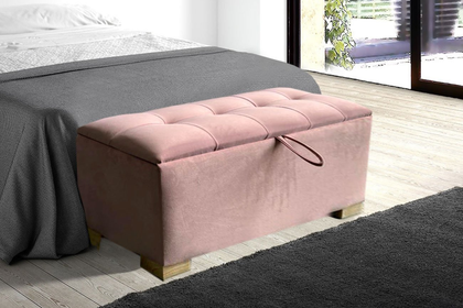 Banco de almacenamiento rosa capitoné a los pies de una cama en un dormitorio luminoso.