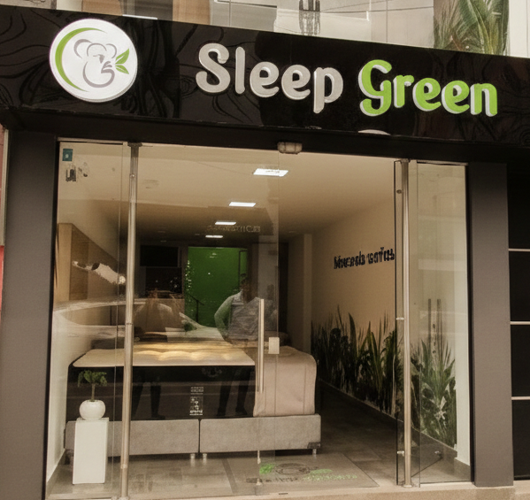 Fachada de Sleep Green con entrada de cristal y exposición de camas en el interior.