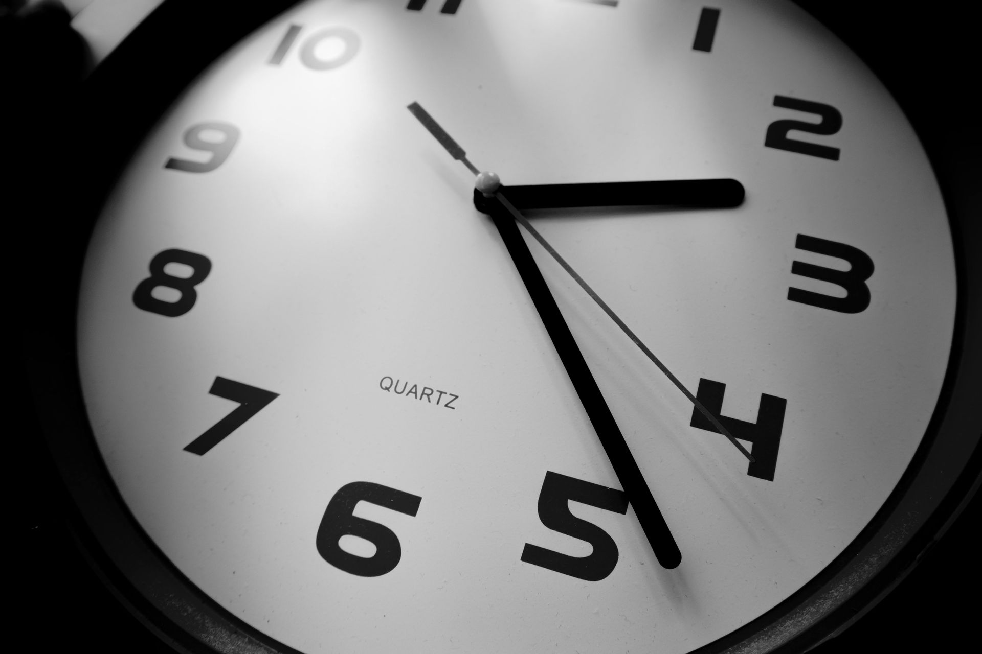 Primer plano de un reloj analógico blanco con números y manecillas negras que marca aproximadamente la 1:25.