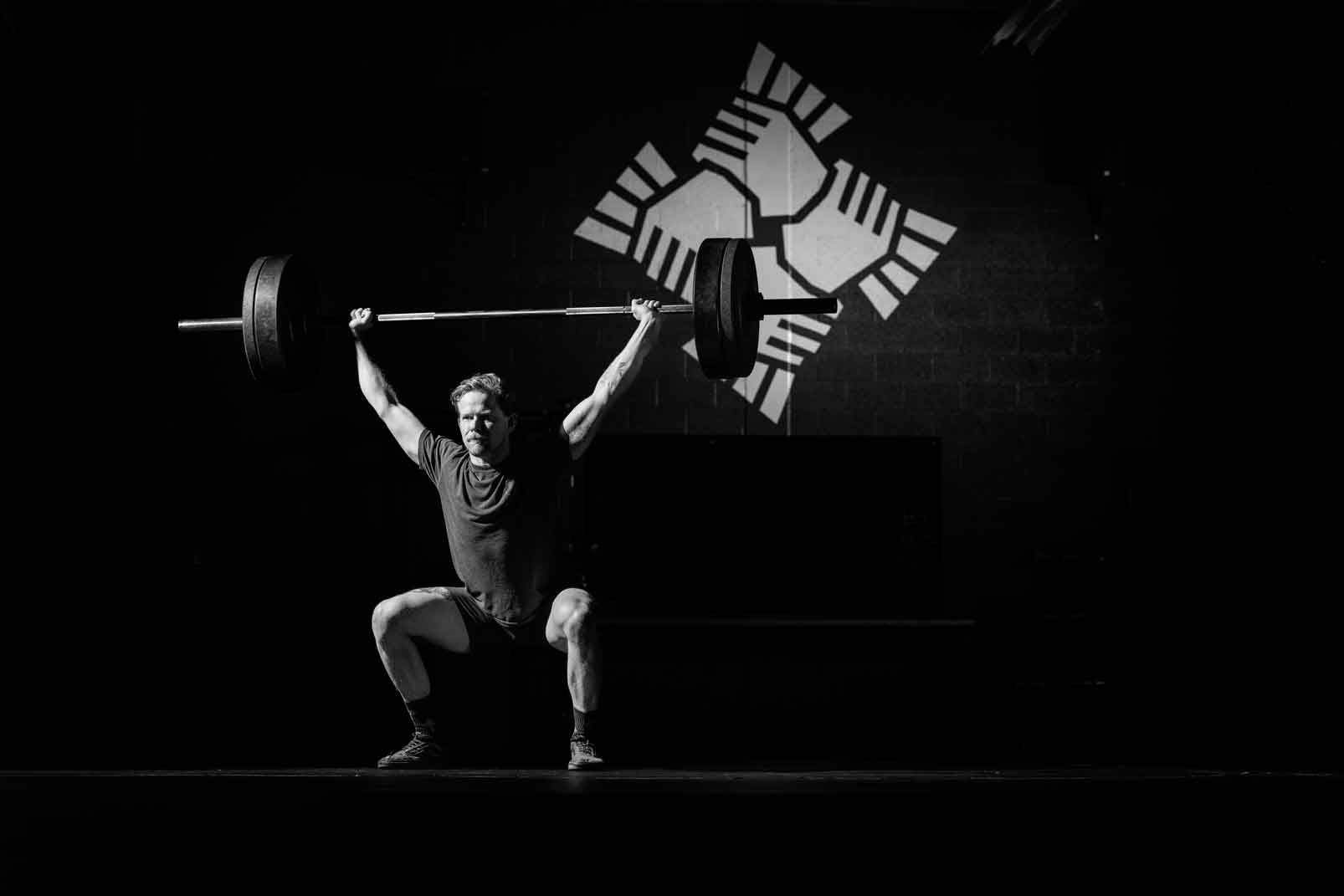 Weightlifter squatting with a barbell overhead under a spotlight on a dark stage