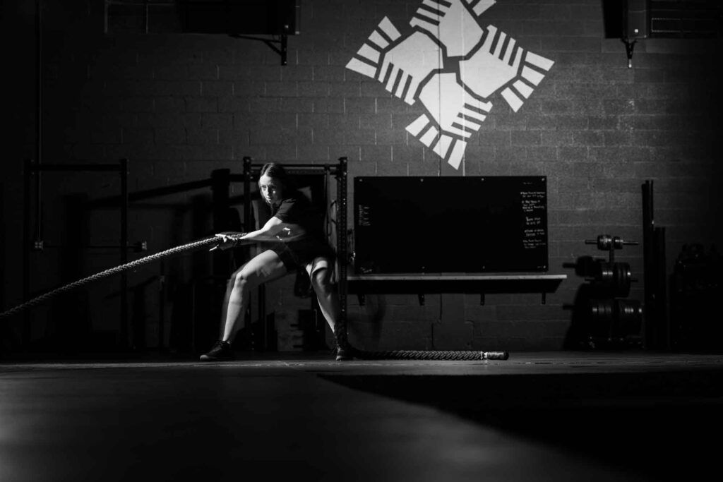 Person in a dim gym in south salt lake swings battle ropes in front of a wall with a white geometric logo.