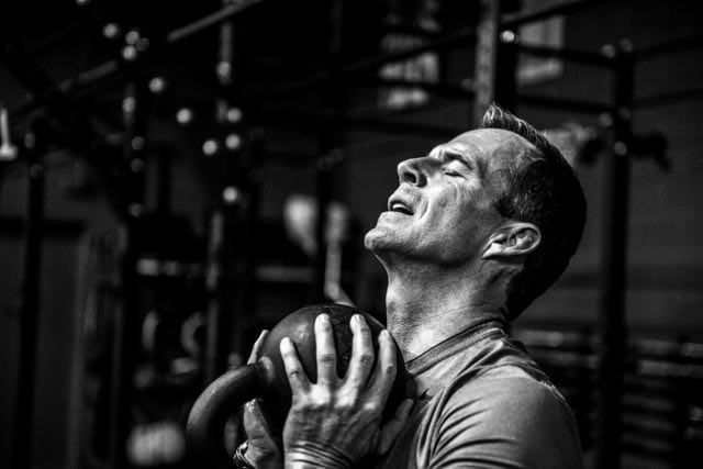 Man lifting a kettlebell in a gym in south salt lake, eyes closed and straining during a workout