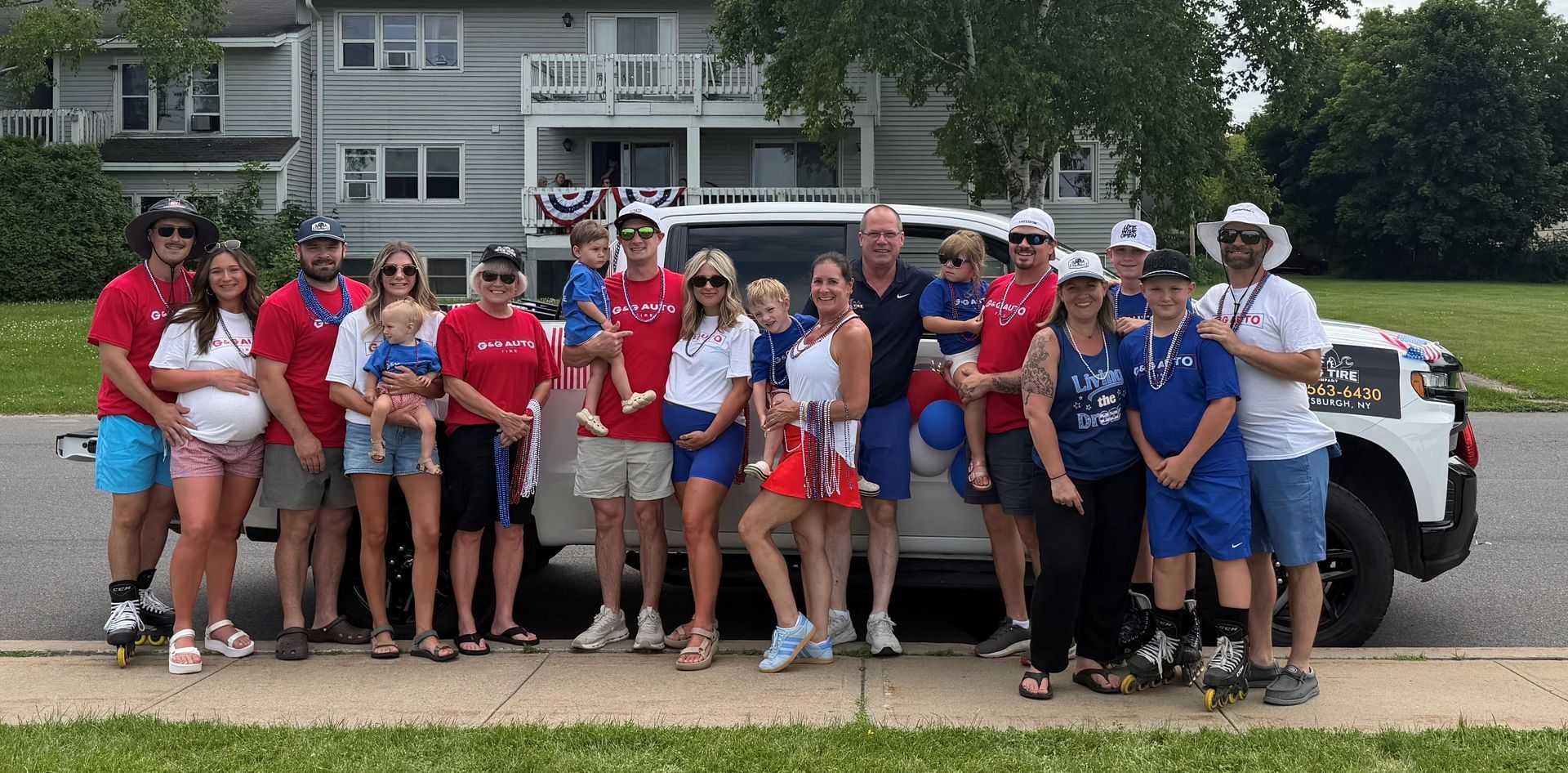 Group of people in red, blue, and white shirts posing in front of parked cars and houses.