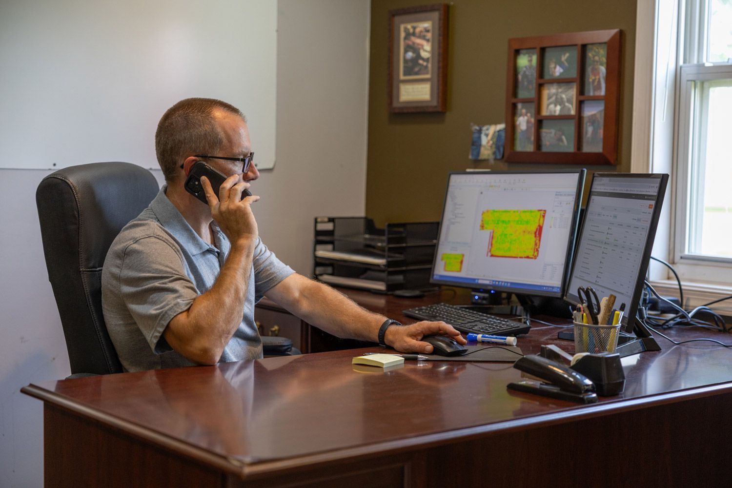A man is sitting at a desk talking on a cell phone.