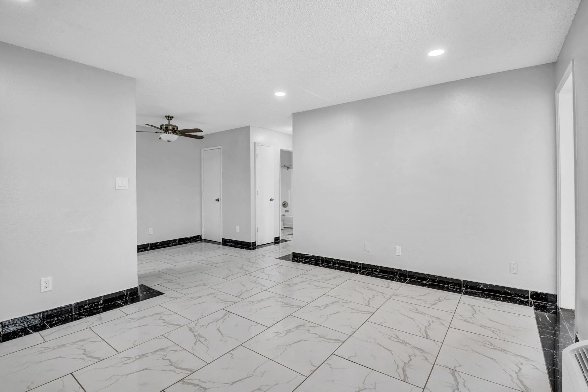 An empty living room with marble tile floors, cone flush roof lighting, and gray walls with a ceiling fan. 