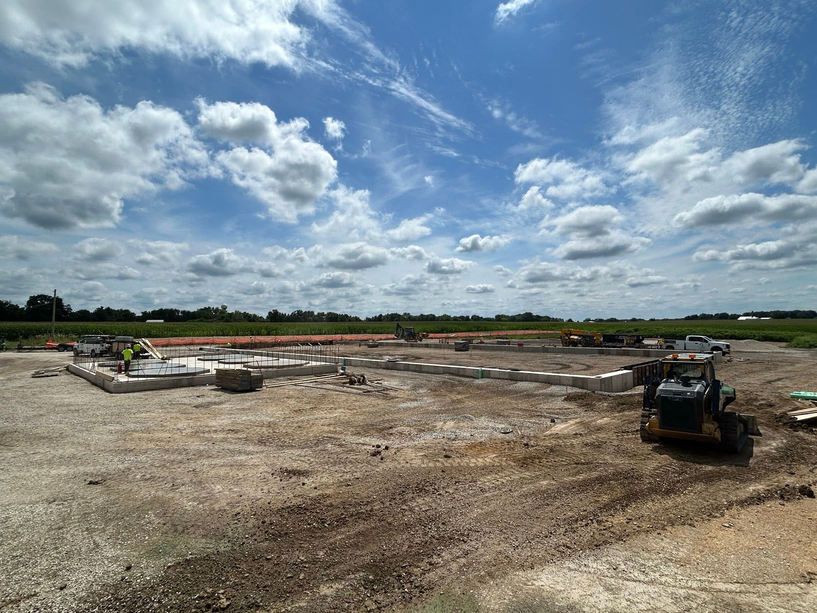 Construction site with foundation and heavy machinery under a cloudy blue sky.