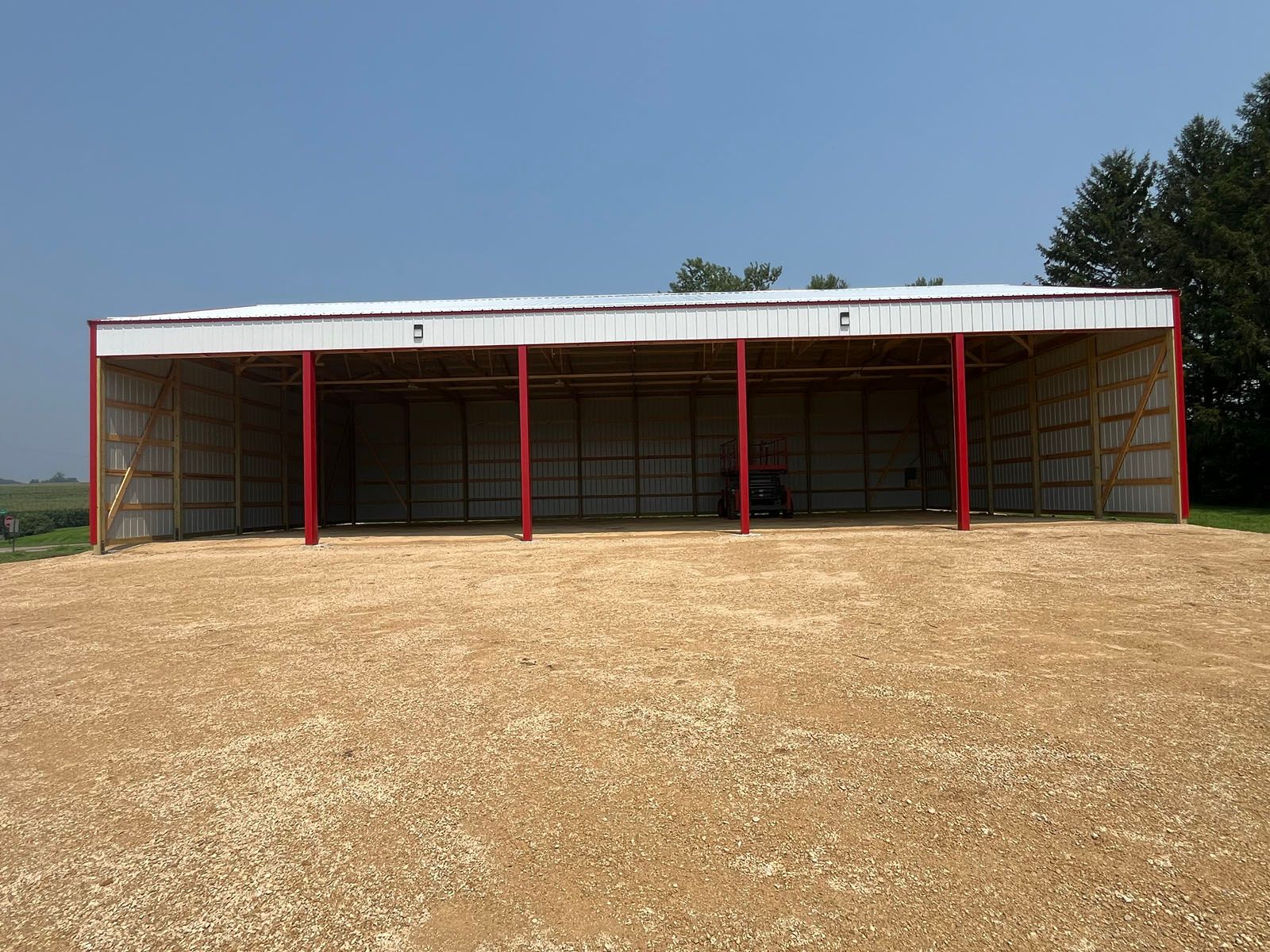 Open-sided barn with red trim, white roof, and gravel ground, under a blue sky.