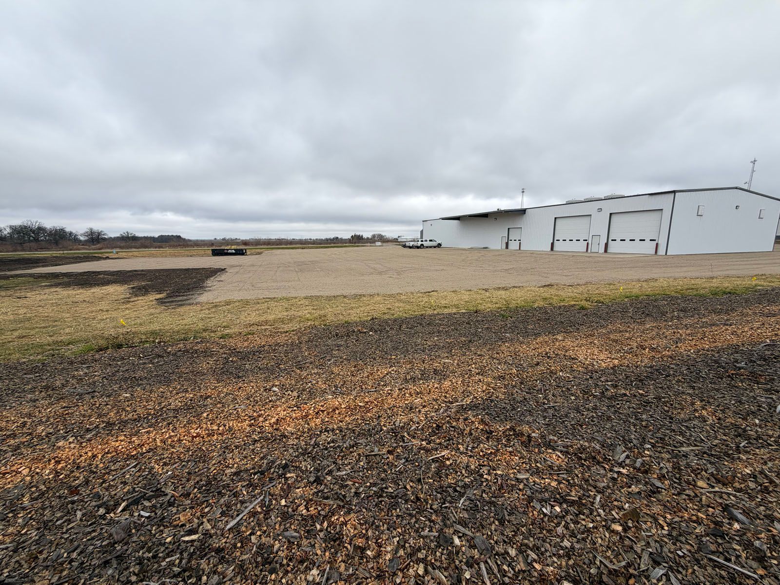 A large white building with loading docks on a gravel lot under a cloudy sky.