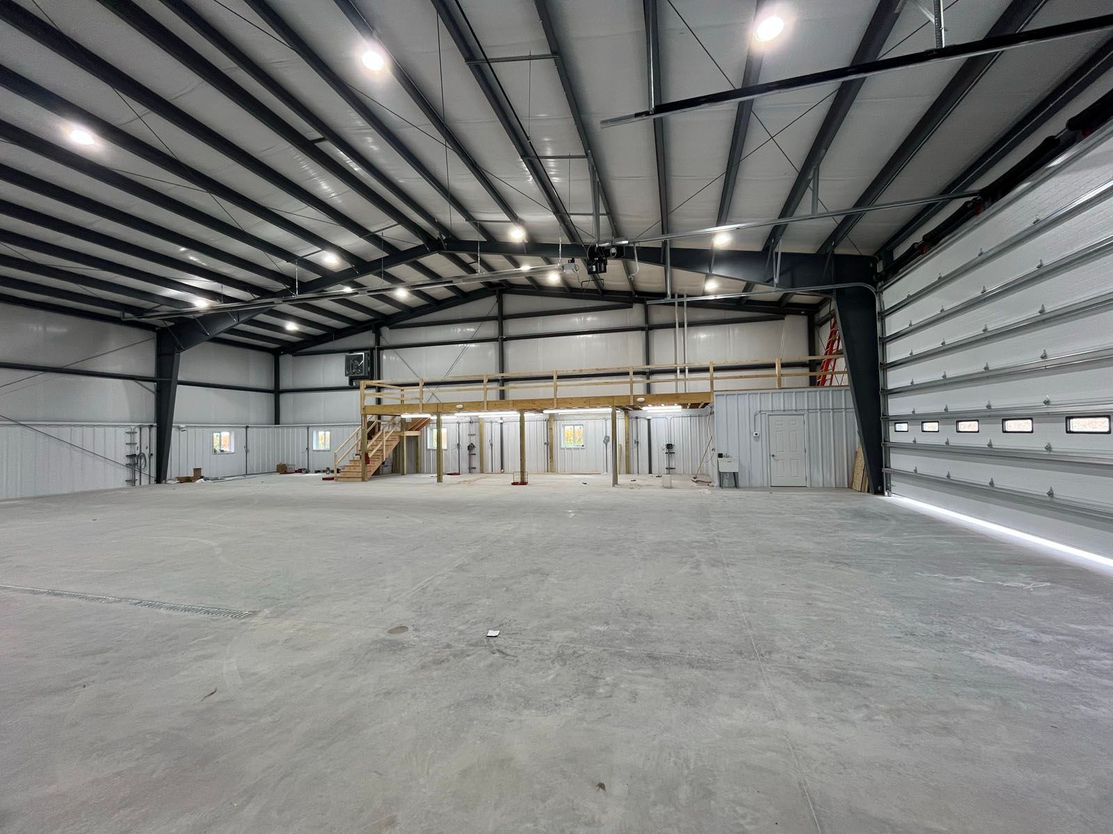 Large, empty industrial warehouse with metal beams and concrete floor; daylight streaming in.