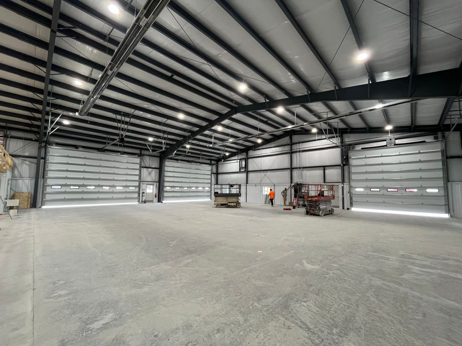 Interior view of an empty warehouse with metal structure, three garage doors, and several overhead lights.