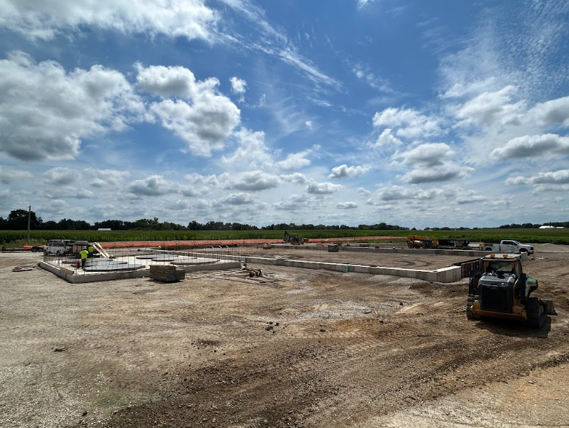 Construction site with concrete foundation walls, machinery, and a cloudy sky.
