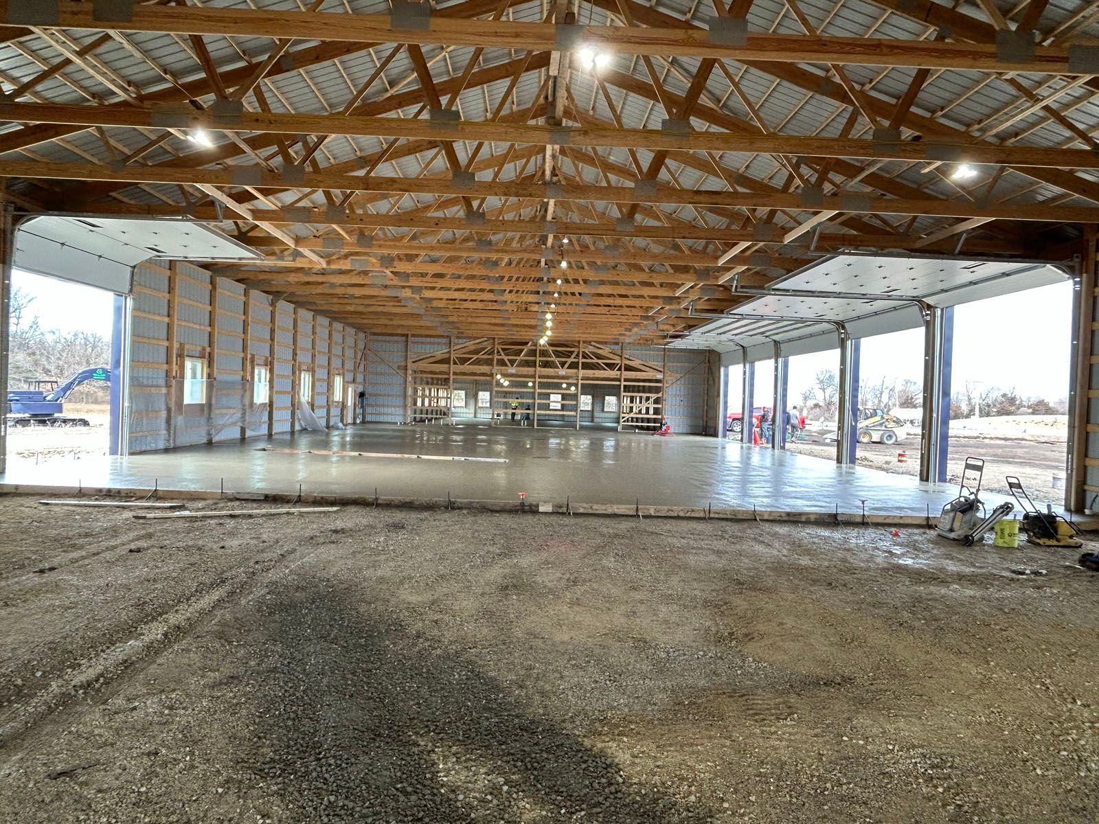 Interior of a large unfinished building with concrete floor and wooden beams; open garage door openings.