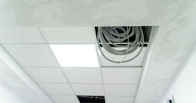 White ceiling tiles with two missing, revealing wires and lighting.