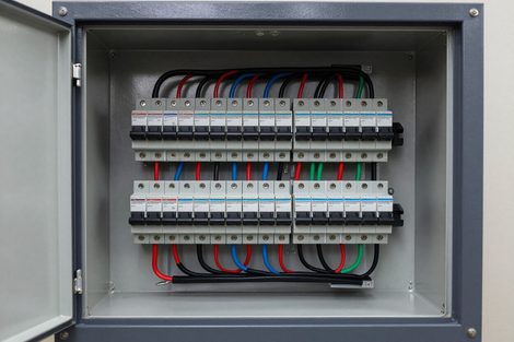 Electrical panel with rows of circuit breakers and multicolored wires inside a metal cabinet