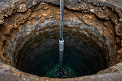 A deep circular well with rough stone walls and a metal pole descending into dark water.