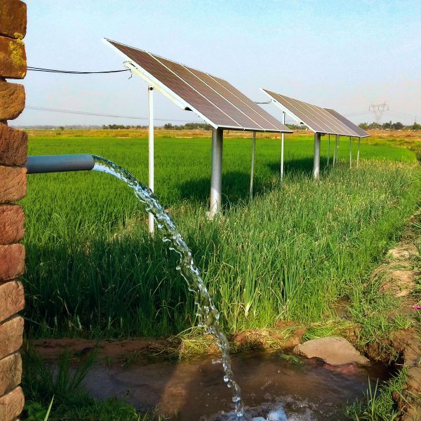 Solar panels pumping water into a green field beside an irrigation canal