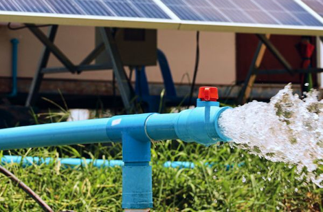 Blue irrigation pipe spraying water onto grass near solar panels