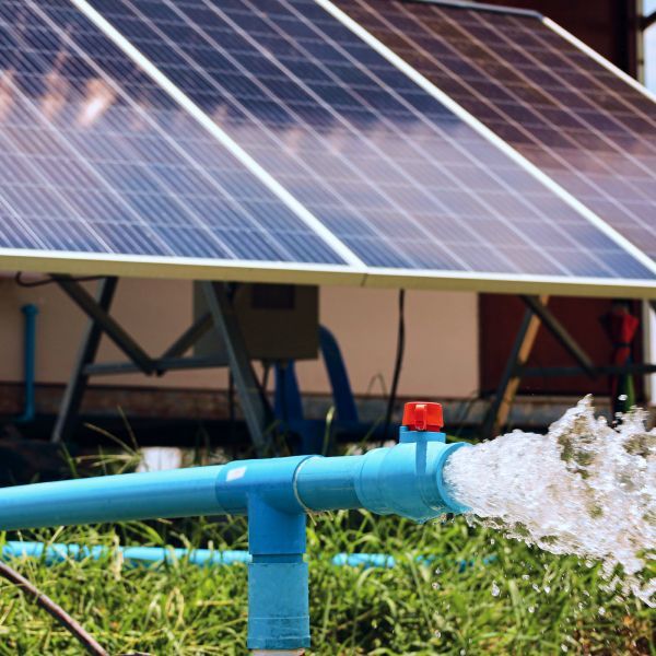 Blue irrigation pipe spraying water in front of solar panels outdoors