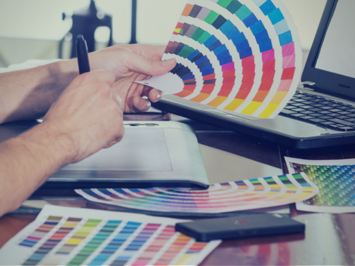 A person is holding a color swatch in front of a laptop