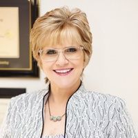 A woman wearing glasses and a necklace is smiling for the camera.