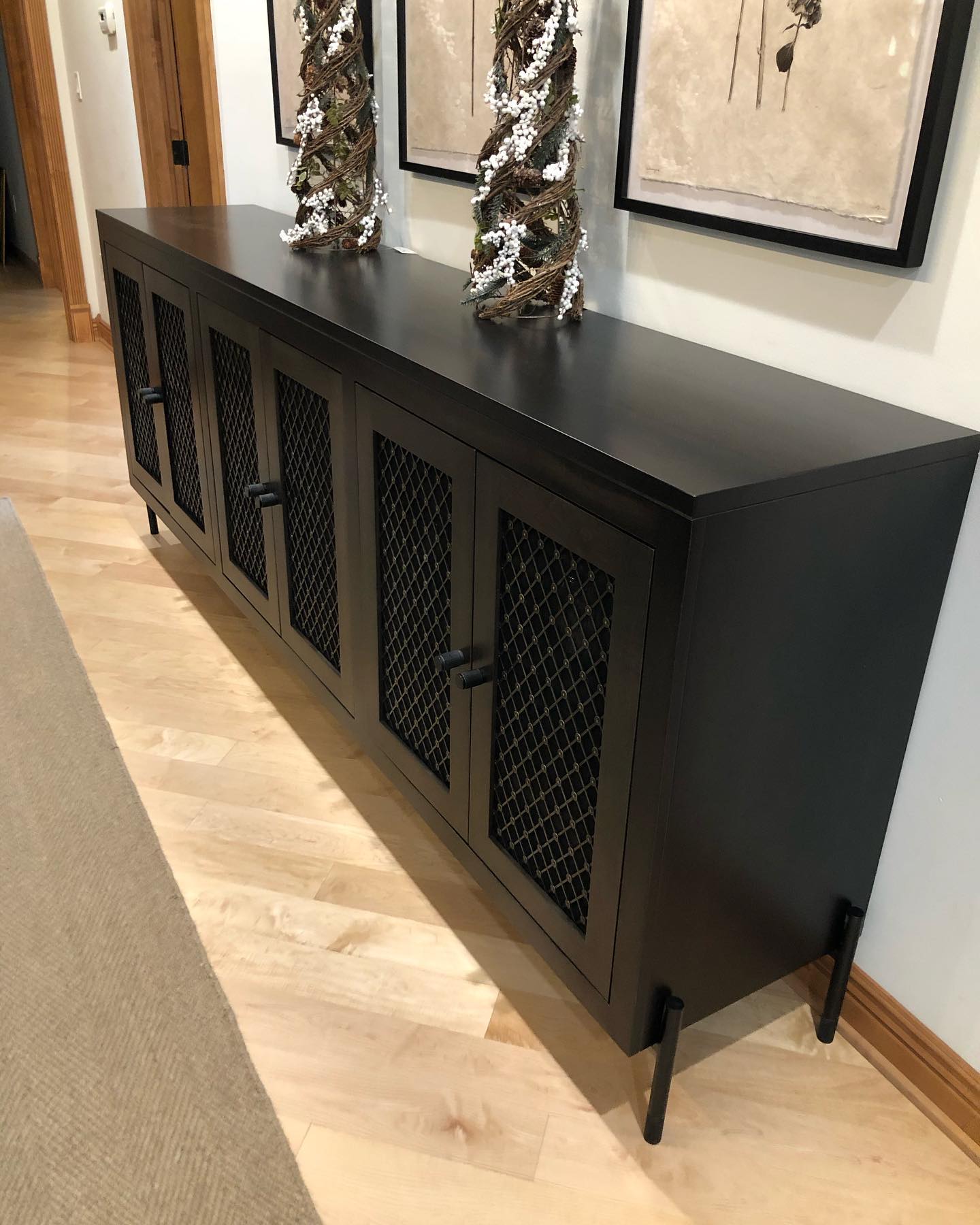 Black metal console cabinet with mesh doors and decorative sculptures in a hallway