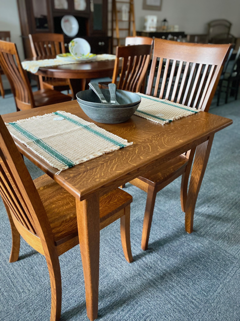 Wooden dining table with two chairs, placemats, and a bowl in a home dining room.