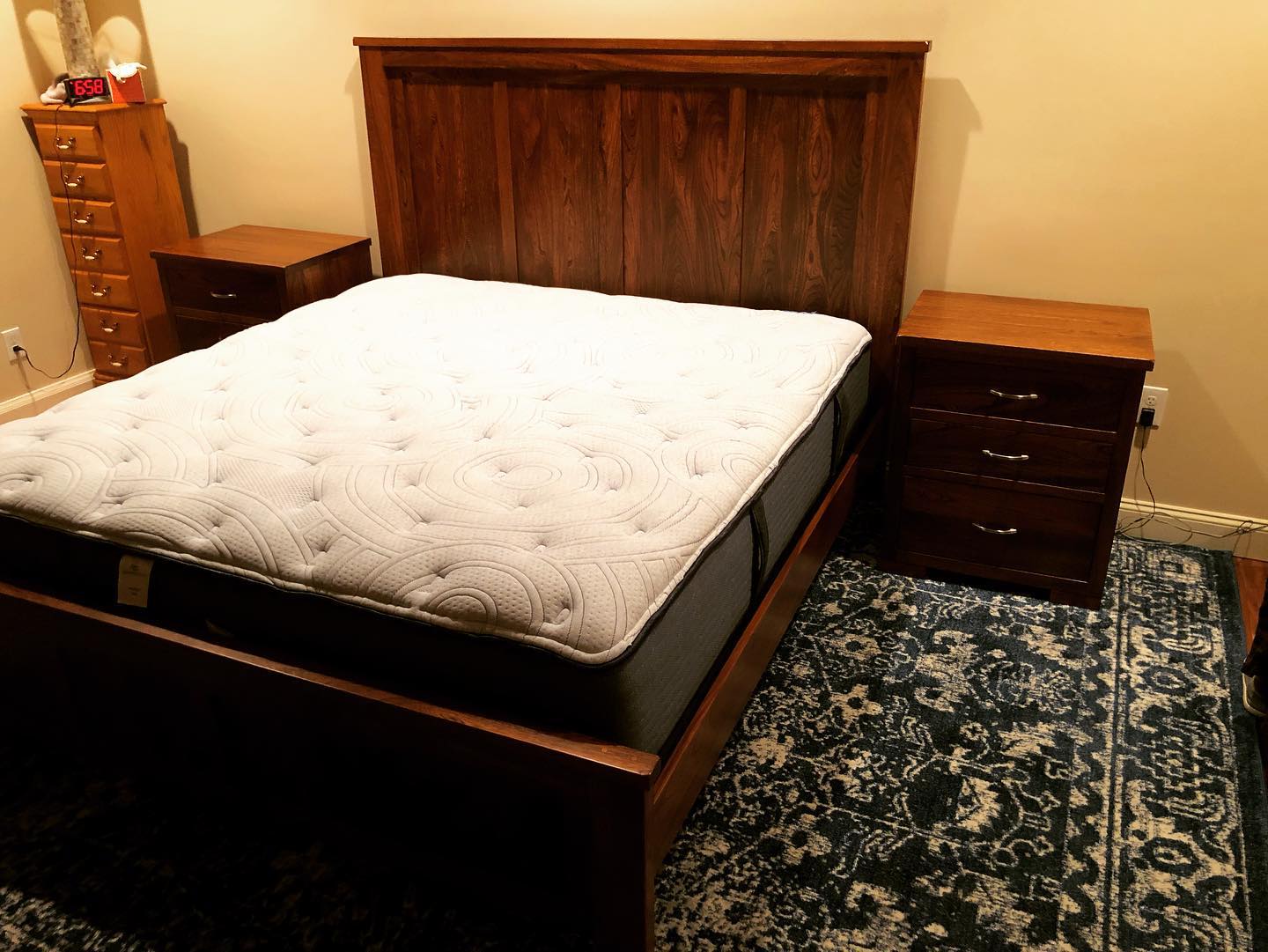 Wooden bed with white comforter in a bedroom, flanked by matching nightstands and a patterned rug.