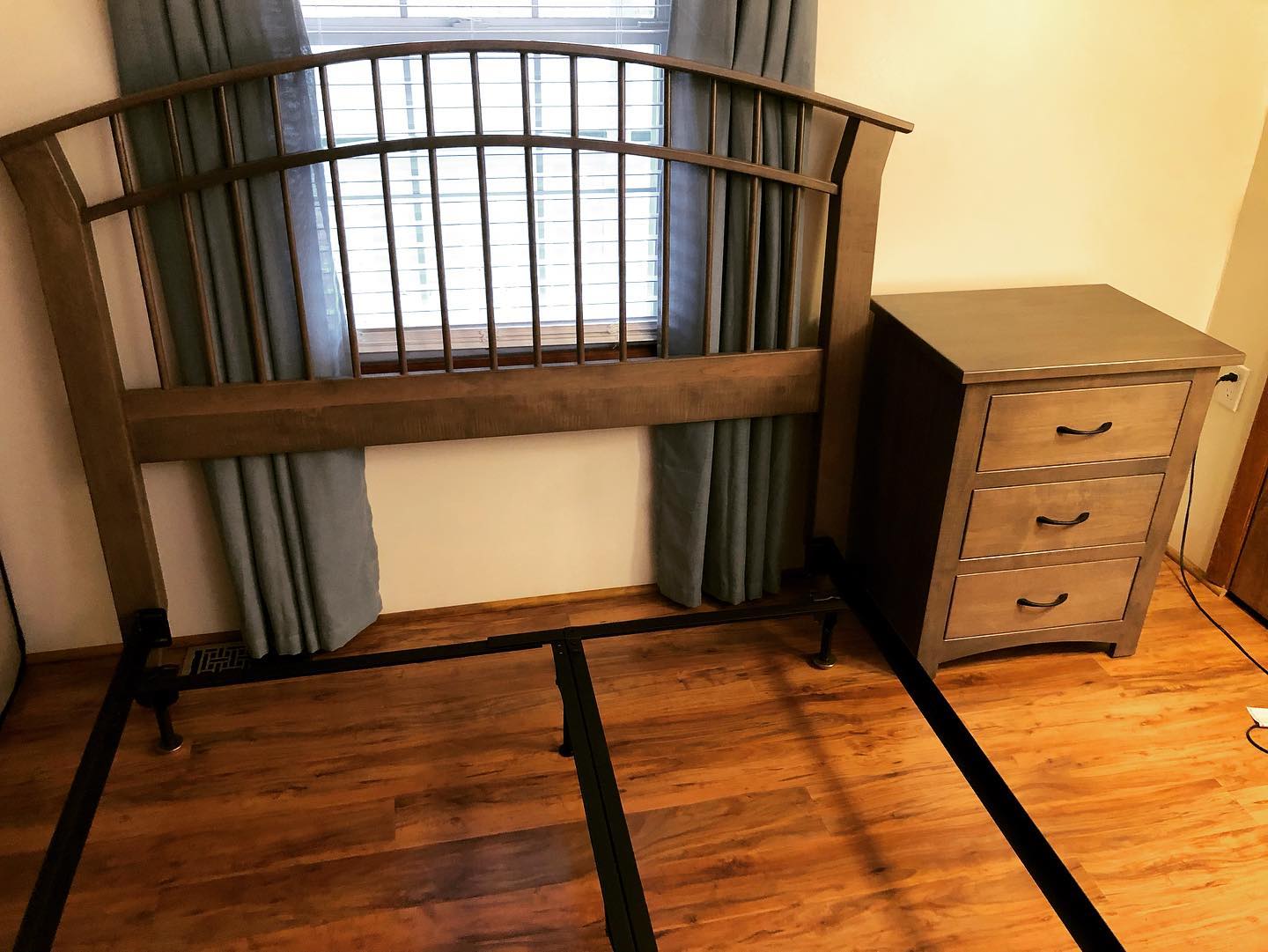 Empty bedroom with a wooden bed frame and a small dresser on hardwood floors.