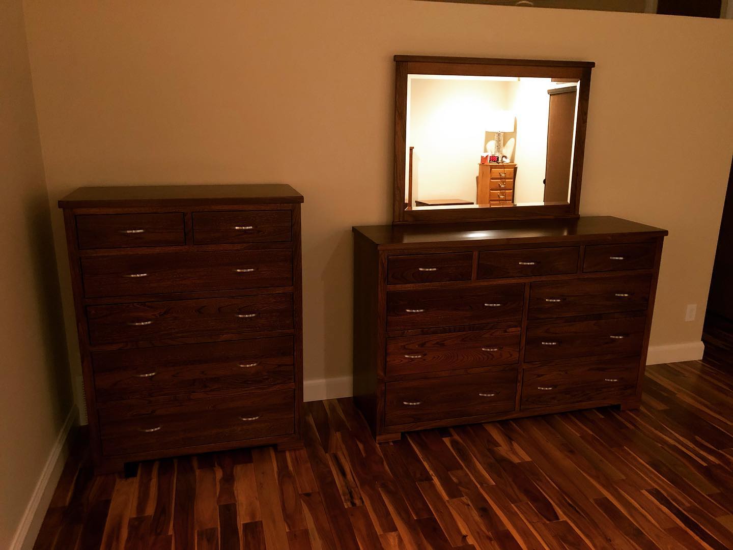 Two dark wood dressers on hardwood floor, one with a mirror against a beige wall.